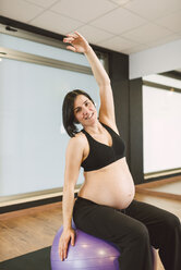 Pregnant woman doing Pilates exercises with gym ball in a gym - RAEF000840