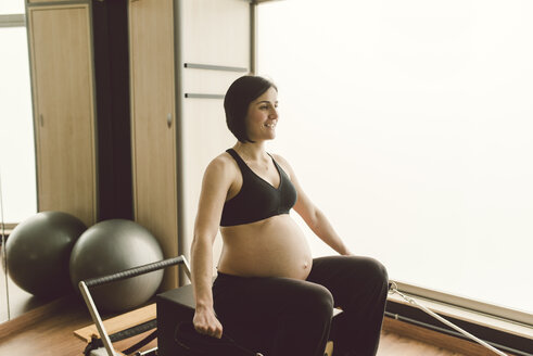 Schwangere Frau macht Pilates-Übungen mit einem Reformer-Pilates-Gerät in einem Fitnessstudio - RAEF000849