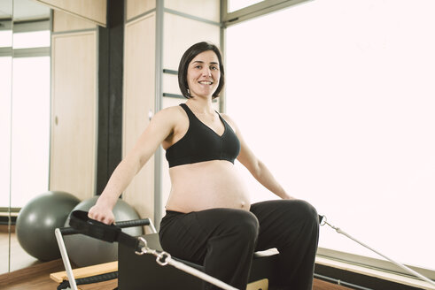 Schwangere Frau macht Pilates-Übungen mit einem Reformer-Pilates-Gerät in einem Fitnessstudio - RAEF000850