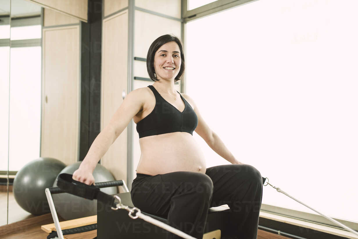 Side view of fit woman doing legs exercise with resistance ropes on Pilates  reformer in gym