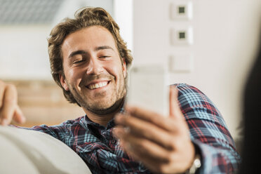 Porträt eines lachenden jungen Mannes, der auf sein Smartphone schaut - UUF006471