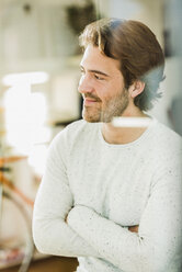 Portrait of relaxed young man with crossed arms standing behind windowpane - UUF006479