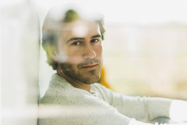 Porträt eines entspannten jungen Mannes, der durch eine Fensterscheibe schaut - UUF006481