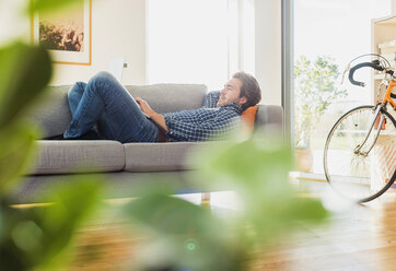 Junger Mann auf der Couch liegend mit Laptop - UUF006484