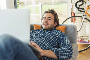 Porträt eines jungen Mannes, der auf der Couch liegt und einen Laptop benutzt - UUF006485