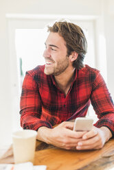 Portrait of laughing man with smartphone at home - UUF006515