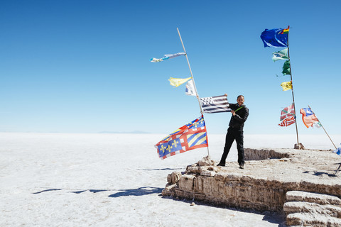 Bolivien, Atacama, Altiplano, Salar de Uyuni, Flaggen aller Länder, Mann hält eine Flagge, lizenzfreies Stockfoto