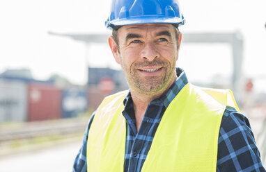 Portrait of confident man wearing hard hat at container port - UUF006524