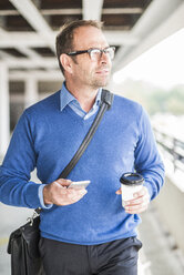 Businessman with cell phone and coffee to go on the move - UUF006533