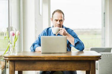 Businessman at home with laptop at wooden table - UUF006538