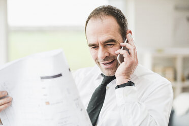 Businessman holding plan and talking on cell phone - UUF006549