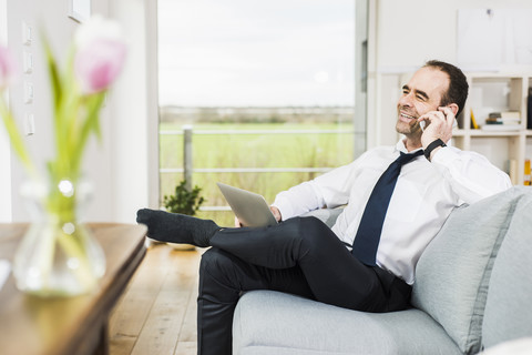 Glücklicher Geschäftsmann auf der Couch, der mit seinem Handy telefoniert, lizenzfreies Stockfoto