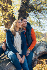 Glückliches Paar genießt den Herbst in einem Wald auf einem Baumstamm sitzend - CHAF001571