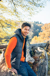 Portrait of smiling young man in a forest on trunk - CHAF001574