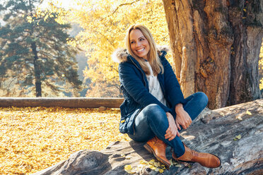 Glückliche Frau genießt den Herbst in einem Wald auf einem Baumstamm sitzend - CHAF001582