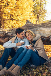 Lächelndes Paar mit Tassen im Herbstwald - CHAF001593
