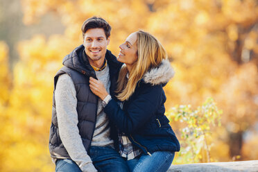 Happy couple enjoying autumn in a forest sitting on a trunk - CHAF001615