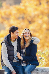 Happy couple enjoying autumn in a forest sitting on a trunk - CHAF001616