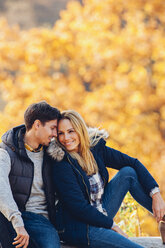 Glückliches Paar genießt den Herbst in einem Wald auf einem Baumstamm sitzend - CHAF001619