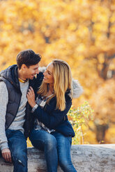 Happy couple enjoying autumn in a forest sitting on a trunk - CHAF001620