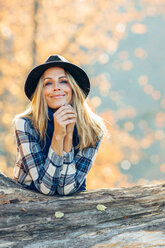 Smiling woman wearing a hat leaning on a trunk - CHAF001626