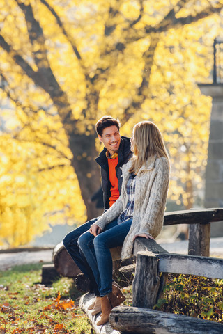 Glückliches Paar sitzt auf einem Holzgeländer in einem herbstlichen Park, lizenzfreies Stockfoto