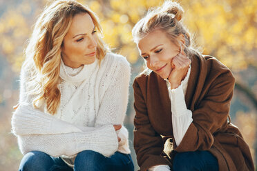 Mother and adult daughter sitting side by side in autumn - CHAF001645