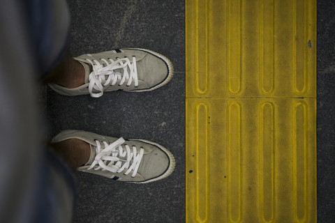 Füße eines Mannes, der vor einer gelben Warnbarkeitslinie steht, lizenzfreies Stockfoto