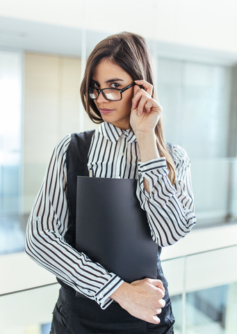 Porträt einer jungen Frau mit schwarzer Akte in einem Büro, lizenzfreies Stockfoto
