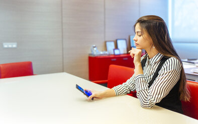 Geschäftsfrau, die in einem Konferenzraum sitzt und auf ihr Smartphone schaut - MGOF001348
