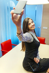 Portrait of smiling businesswoman taking selfie with smartphone in a conference room - MGOF001350
