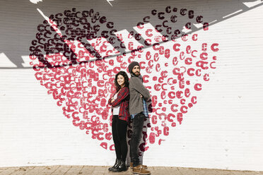 Junges Paar steht Rücken an Rücken vor einer Backsteinmauer mit einem Herz - JRFF000404