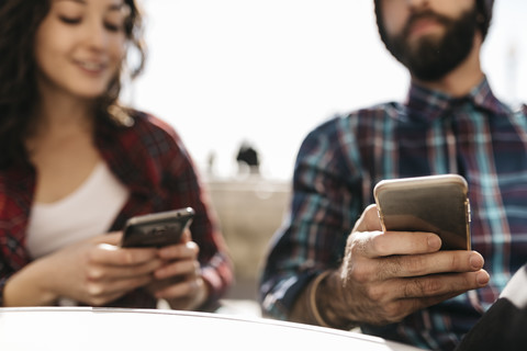 Junges Paar benutzt sein Handy in einem Straßencafé, lizenzfreies Stockfoto