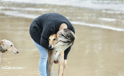 Spanien, Llanes, junge Frau küsst ihren Windhund am Strand - MGOF001369