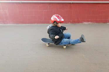 Kleiner Junge mit Schutzhelm auf einem Skateboard sitzend - VABF000136