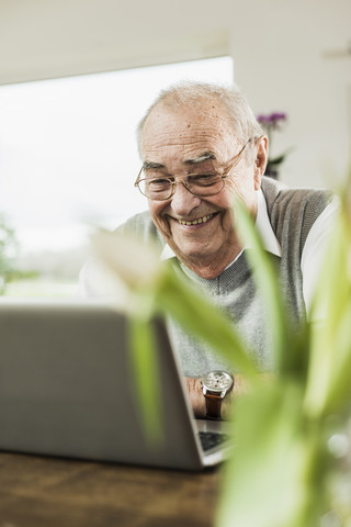 Porträt eines glücklichen älteren Mannes, der zu Hause einen Laptop benutzt, lizenzfreies Stockfoto