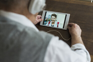 Senior man using mini tablet and headphones for skyping with his grandson - UUF006571