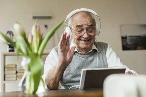 Älterer Mann benutzt Mini-Tablet und Kopfhörer zum Skypen zu Hause - UUF006573
