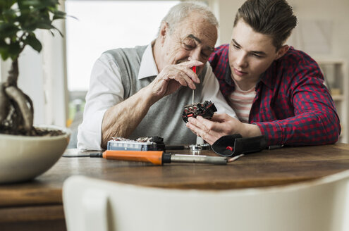 Älterer Mann repariert zusammen mit seinem Enkel eine Spielzeugeisenbahn - UUF006584