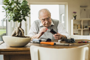 Senior man repairing toy train at home - UUF006588