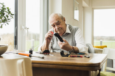 Senior man repairing toy train at home - UUF006589