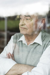 Porträt eines nachdenklichen älteren Mannes mit verschränkten Armen, der durch ein Fenster schaut - UUF006593