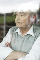 Portrait of pensive senior man with crossed arms looking through window - UUF006593