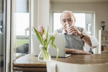 Porträt eines älteren Mannes mit Laptop, der zu Hause ein Glas Wasser trinkt - UUF006606