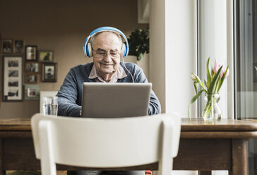 Älterer Mann mit Laptop und Kopfhörern zu Hause - UUF006609