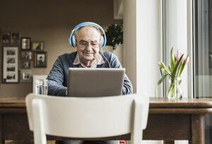 Älterer Mann mit Laptop und Kopfhörern zu Hause - UUF006609