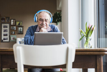 Älterer Mann mit Laptop und Kopfhörern zu Hause - UUF006610