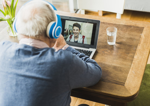 Älterer Mann benutzt Laptop und Kopfhörer, um mit seinem Enkel zu skypen, lizenzfreies Stockfoto