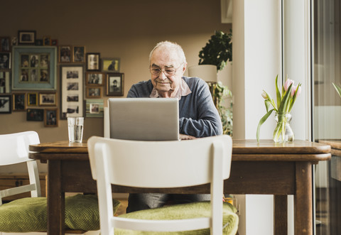 Älterer Mann sitzt am Tisch im Wohnzimmer und benutzt einen Laptop, lizenzfreies Stockfoto