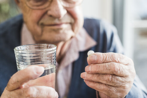 Die Hände eines älteren Mannes halten eine Tablette und ein Glas Wasser, Nahaufnahme - UUF006618